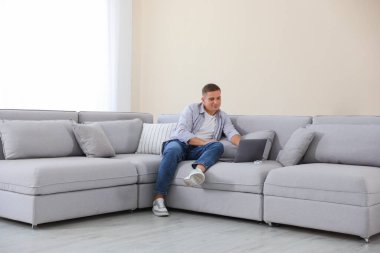 Evde kanepede dizüstü bilgisayar kullanan genç adam