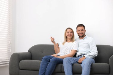 Evdeki kanepede klima kontrol etmek için uzaktan kumanda kullanan çift. Metin için boşluk