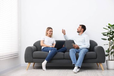 Evdeki koltukta uzaktan kumandayla klima kullanan çift.