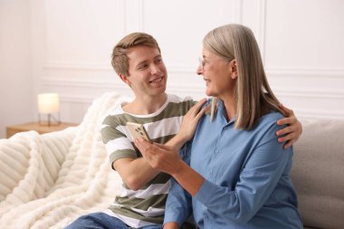 Mutlu oğul ve annesi evdeki kanepede akıllı telefon kullanıyor.