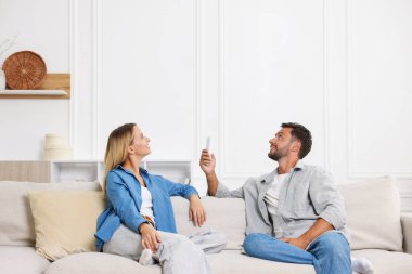 Evdeki koltukta uzaktan kumandayla klima kullanan çift.