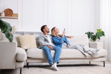 Evdeki koltukta uzaktan kumandayla klima kullanan çift.