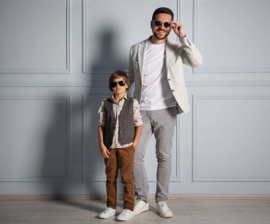 Baba ve oğul şık kıyafetler içinde ışık duvarının yanında poz veriyorlar.