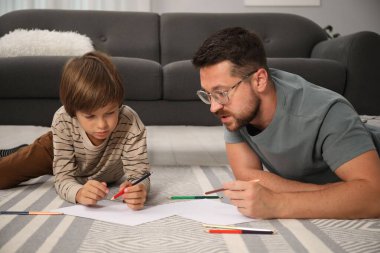 Baba ve oğul evde yerde birlikte çiziyorlar.