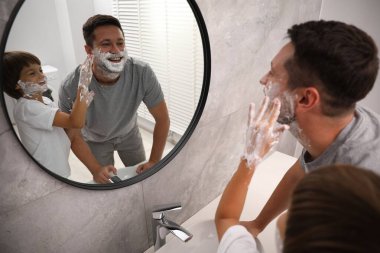 Banyoda yüzlerinde tıraş köpüğü olan baba ve oğul.