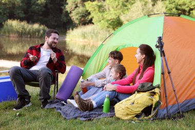 Mutlu bir aile kamp çadırı, turistik malzemeler ve nehir kenarında içki molası veriyor.