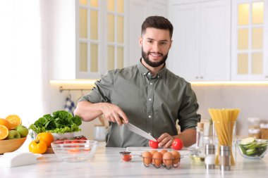 Yemek pişirme süreci. Gülümseyen adam mutfakta domates kesiyor.