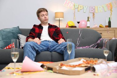 Adam partiden sonra dağınık bir odada kanepede akşamdan kalma.