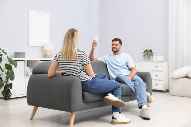 Evdeki koltukta uzaktan kumandayla klima kullanan çift.