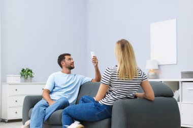 Evdeki koltukta uzaktan kumandayla klima kullanan çift.