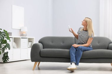 Evdeki kanepede uzaktan kumandayla klima kullanan bir kadın. Metin için boşluk