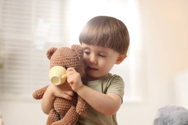 Küçük şirin çocuk içeride oyuncak ayısıyla çay partisi yapıyor.