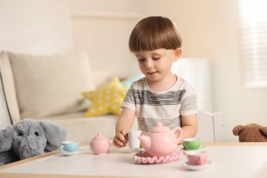 Oyuncak fili ile evde çay partisi yapan sevimli küçük çocuk.
