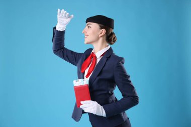 Pasaportu ve açık mavi arka planda biletleri olan gülümseyen hostes.