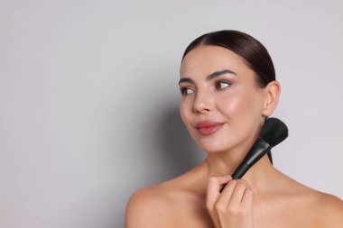 Açık gri arkaplanda makyaj fırçası olan güzel kadın, metin için boşluk