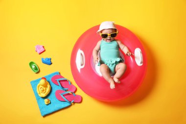 Güneş gözlüklü şirin bir bebek. Şişirilebilir yüzüğü ve sarı arka planda plaj aksesuarları var.