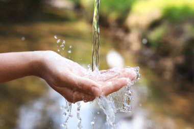 Su kavramını sakla. Nehrin kenarında, temiz suyun altında elini tutan kadın, yakın plan.
