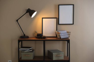 Stylish lamp, other decor and books on console table near beige wall indoors