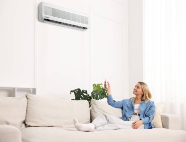 Evdeki koltukta uzaktan kumandayla klima kullanan bir kadın.