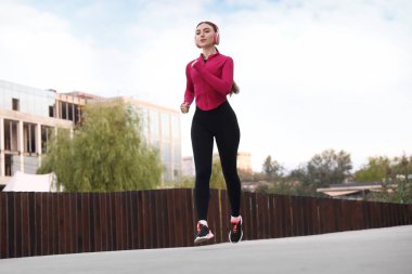 Kulaklıklı güzel bir kadın açık havada koşuyor, düşük açılı.