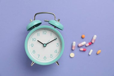 Menopoz. Alarm saati ve mor arka planda haplar, düz uzanma