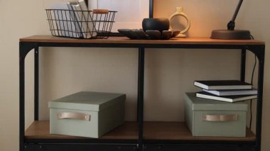 İçerideki bej duvarın yanında şık lamba, dekor ve kitaplarla konsol masası. Kamera yukarı çıkıyor.