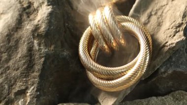 Kayalarda duman içinde şık altın küpeler, yakın plan. Kamera yukarı hareket ediyor