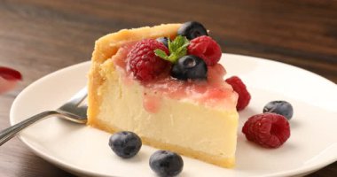 Ahşap masada meyveli ve soslu lezzetli cheesecake yiyen kadın, yakın plan.