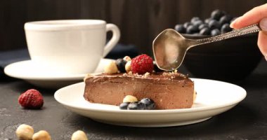 Kadın, siyah masada fındıklı ve dutlu lezzetli çikolatalı kek yiyor.