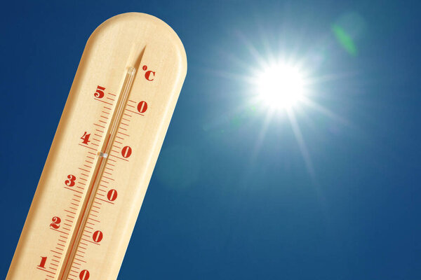 Термометр, показывающий высокую температуру против неба с ярким солнцем. Очень жаркая погода