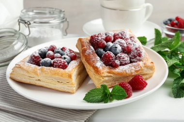 Böğürtlenli, pudra şekerli ve naneli börekler beyaz masada, yakın plan.