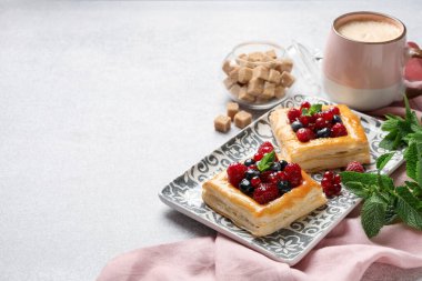 Açık gri masada böğürtlenli, naneli, esmer şekerli ve kahveli börekler, yakın plan. Metin için boşluk