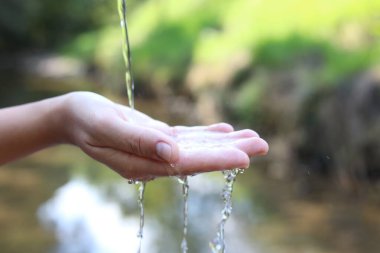 Su kavramını sakla. Nehrin kenarında, temiz suyun altında elini tutan kadın, yakın plan.