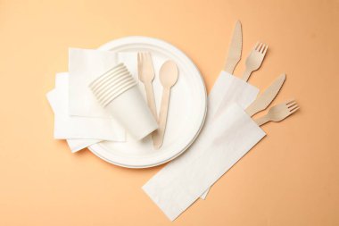 Set of disposable tableware on pale orange background, flat lay