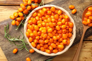 Hasır kasede taze deniz dikenli üzümleri ve ahşap masada yapraklar.