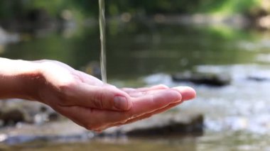 Su kavramını sakla. Nehrin kenarında, temiz suyun altında elini tutan kadın, yakın plan.