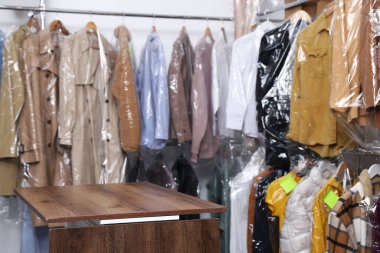Kuru temizleme servisi. Birçok farklı giysi plastik poşetlerde raflarda ve ahşap tezgahlarda kapalı alanlarda