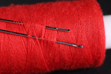 Siyah arkaplanda dikiş iğneleri olan kırmızı iplik makarası, makro görünüm