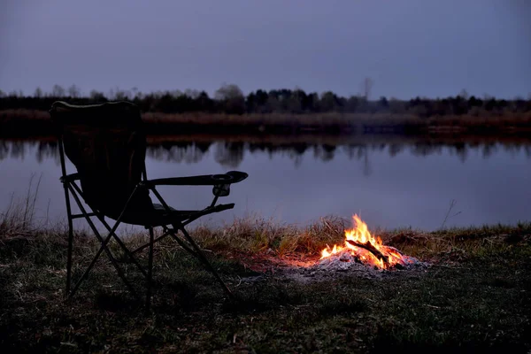 Tourist chair, folding chair, bonfire on the river bank in late evening, twilight in the fall at sunset, relaxation and rest, early autumn, close-up,  blur as an artistic effect, copy space