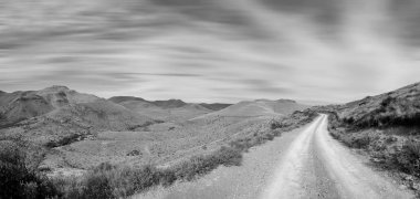 kırsal yol ve Eastern Cape Dağları bulutlu gökyüzü arka plan üzerinde siyah beyaz fotoğraf  