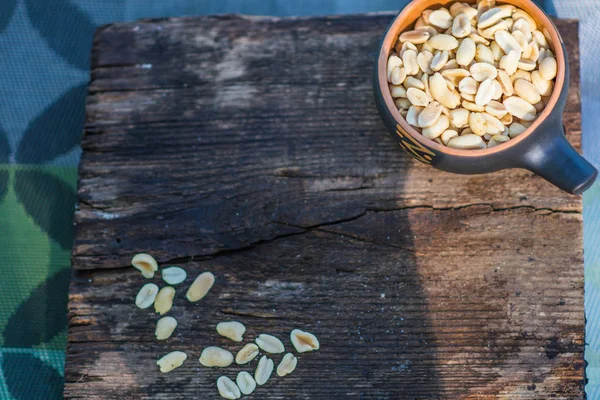 Crunchy, fried and salted peanuts, peeled. A nutritious snack in a small kerimic pot on the background of a natural brown tree with a natural pattern. Appetizing dish in the fresh air.