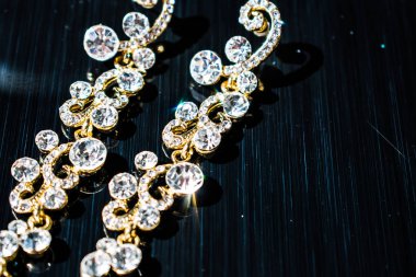 Kulağa altın, sarı küpe. Büyük ve küçük beyaz taşlarla akşam ve zarif süslemeleri. Altın takı ve Bijuteri