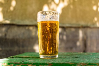 Bir bardak bira alkol ile. Altın, şeffaf bir kupa içki sarhoş edici standları gün ışığı ışınlarının bir ahşap stand. En iyi beyaz ve havadar köpük.