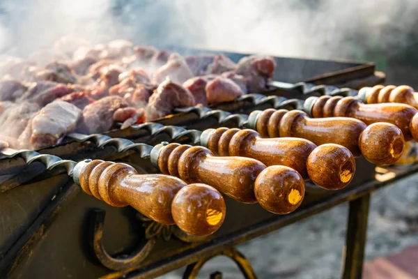 Grilled meat, Golden pork with skewers and wooden handles. A lot of smoke in the process of cooking fragrant meat dishes in nature. Summer kitchen. Raw meat on fire.