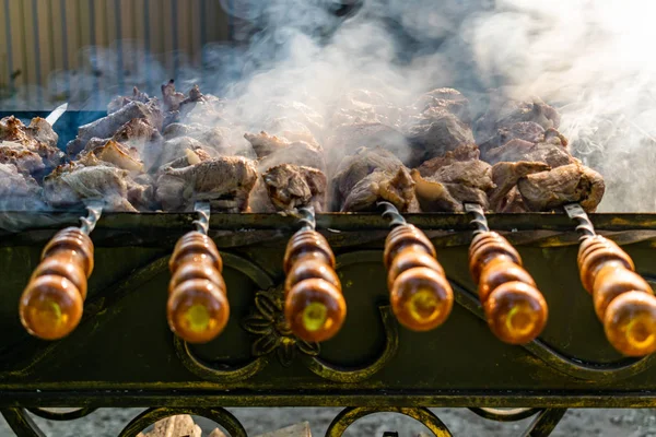 Grilled meat, Golden pork with skewers and wooden handles. A lot of smoke in the process of cooking fragrant meat dishes in nature. Summer kitchen. Raw meat on fire.