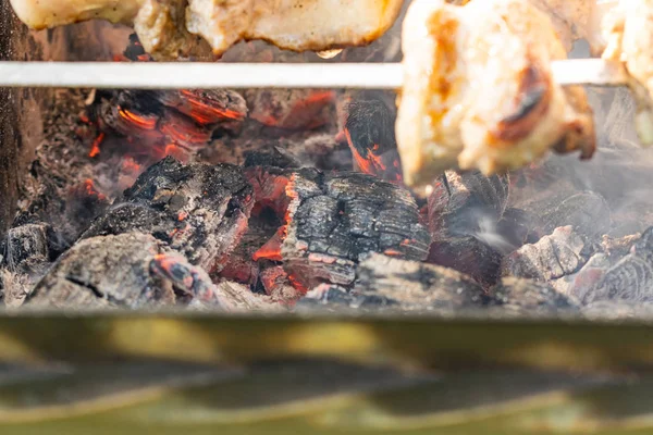 Grilled meat, Golden pork with skewers and wooden handles. A lot of smoke in the process of cooking fragrant meat dishes in nature. Summer kitchen. Raw meat on fire.