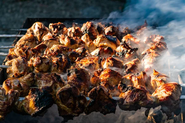 Grilled meat, Golden pork with skewers and wooden handles. A lot of smoke in the process of cooking fragrant meat dishes in nature. Summer kitchen. Raw meat on fire.