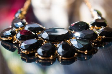 Zarif kolye siyah taşlar ve altın metal bir yansıtıcı siyah ayna yüzey üzerinde temel. Karanlık değerli taşlar damlacıkları ve oval şeklinde. Takı ve aksesuarlar, kadın, moda arka plan tasarımı için.