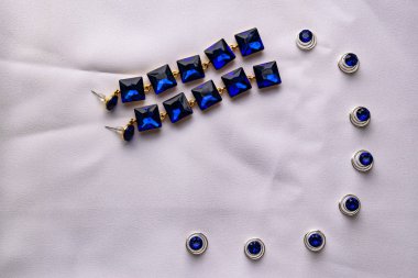 Güzel ve şık takı ve kadınlar için aksesuar. Safir küpe beyaz Tekstil zemin üzerine kare taşlarla. Mavi parlak rhinestones altın Metal temel. Stilettos, küçük çakıl taşları.