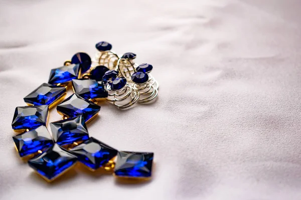 美丽时尚的珠宝和配件为妇女 蓝宝石耳环与方石在白色纺织品背景 金金属基座上的蓝色明亮的水钻 高跟鞋 小鹅卵石 — 图库照片